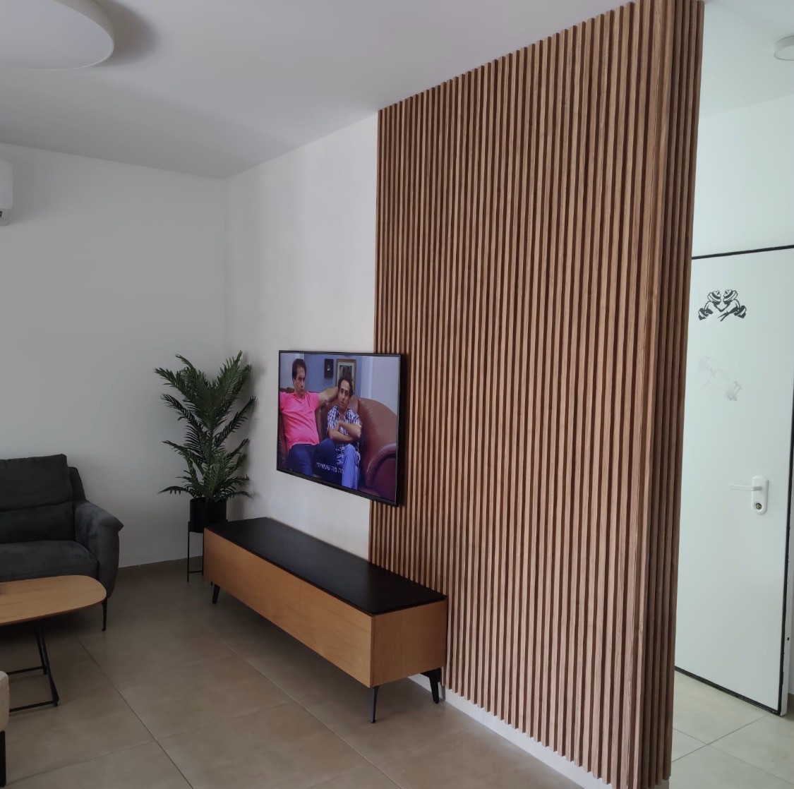 Floor-to-ceiling oak slat panel beside a wall-mounted television in a living room