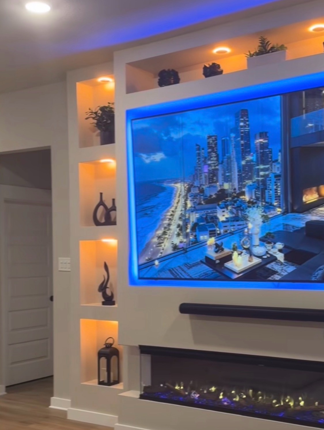 White built-in media wall with a backlit television, downlit display niches and a linear electric fire