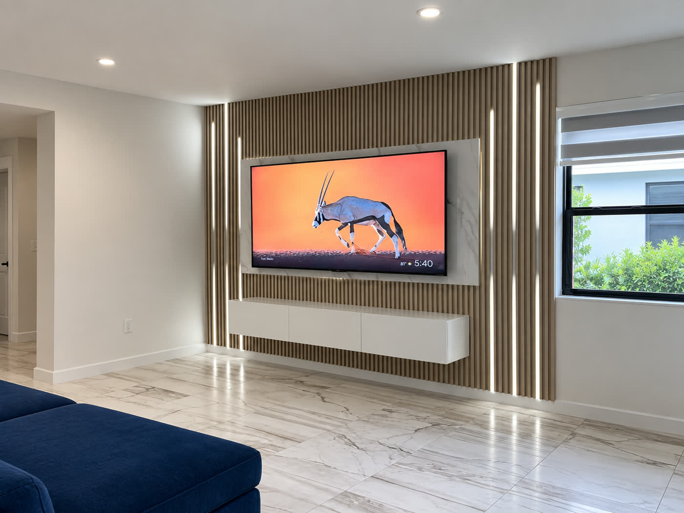 A taupe slat wall with vertical LED reveals either side of a centred television above a white floating console